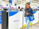 a woman holding a cell phone walking next to a walmart plus sign in store