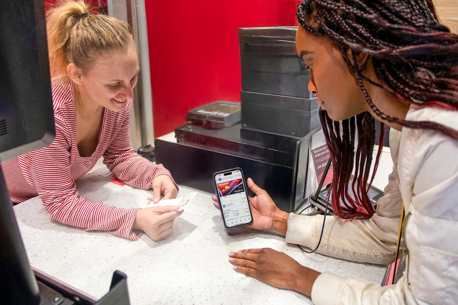 A person showing a phone and a receipt to an employee for a price adjustment at the Target guest service counter.
