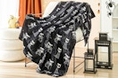 Lifestyle image of the Ways to Celebrate Plush Skull Dogs Throw Blanket on chair with Halloween decorations in the background