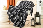 Lifestyle image of the Ways to Celebrate Plush Skull Dogs Throw Blanket on chair with Halloween decorations in the background