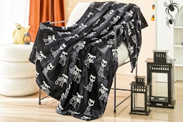 Lifestyle image of the Ways to Celebrate Plush Skull Dogs Throw Blanket on chair with Halloween decorations in the background