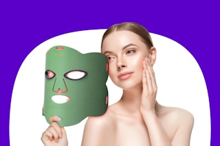 A woman holds a red light therapy mask and touches her face