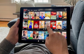 man laying on couch watching netflix through the app on his tablet