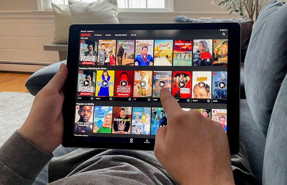 man laying on couch watching netflix through the app on his tablet