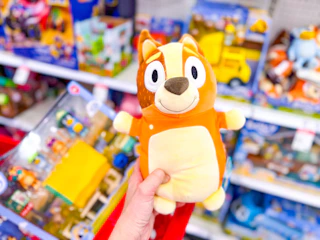 hand holding a bingo squishmallow plush in front of a target cart