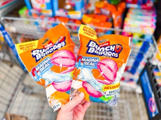 hand holding two bags of bunch o balloons reusable water balloons over walmart cart
