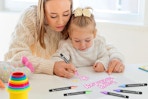 a mom and daughter drawing on a piece of paper with markers
