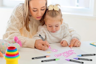 a mom and daughter drawing on a piece of paper with markers