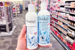 person holding ouidad shampoo and conditioner in an aisle