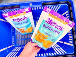 hand holding a bag of miltons crackers over another bag in walmart hand cart