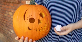 someone holding a carved pumpkin and a battery operated tea light candle