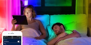 A woman and man laying in bed under rainbow LED lights