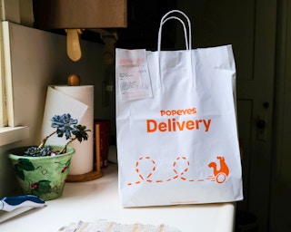 A Popeyes delivery bag sitting on a counter in someone's kitchen.