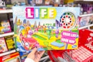 person holding the game of life board game over a target cart