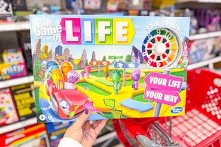 person holding the game of life board game over a target cart