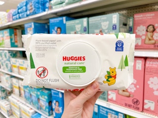 A Huggies wipes package held out by hand in front of other diapers sitting on a store shelf.