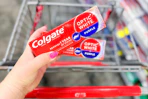 person holding 2 colgate toothpastes over a cart