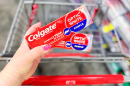 person holding 2 colgate toothpastes over a cart