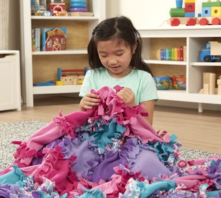 A girl sitting with a colorful quilt in a room