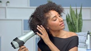 A woman blow drying her hair with a Revlon hair dryer.