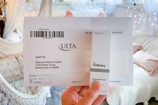 Hand holding a box of The Ordinary skin care product and an online Ulta order receipt.