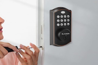 a bronze digital door lock on a door and a person with a screwdriver
