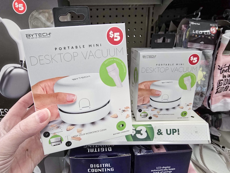 person holding a portable mini desktop vacuum in front of a shelf display