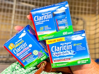 hand holding claritin allergy care products over a shopping cart