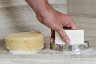 a hand on a bar of soap in a soap dish next to a sponge
