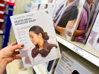 hand holding a sharper image heated wrap in front of a target shelf