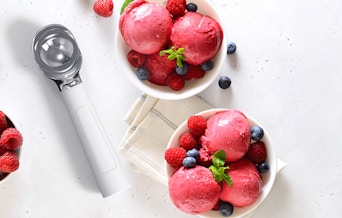 an ice cream scooper next to a bowl of ice cream with fruit
