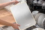 Person holding the COOKEERS Stainless Steel Cutting Board by a dish washing machine.