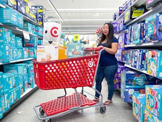 a woman standing behind a target cart that is filled with diapers with a welcome bag on top