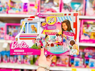 hand holding a barbie clinic and ambulance in front of a target shelf