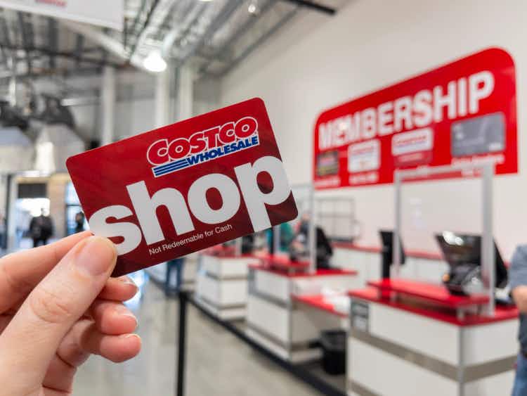A person's hand holding up a Costco Shop card near the the membership counter.