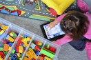 A child using a drawing app on an iPad while sitting on the floor of a playroom