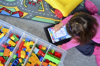 A child using a drawing app on an iPad while sitting on the floor of a playroom