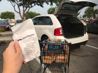 hand holds a receipt in front of car with open trunk at an albertsons store