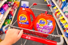 person pushing a cart with tide pods and liquid detergent in it