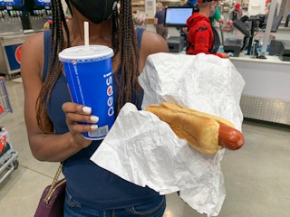 A woman holding a beverage cup and a hotdog near the Costco food court.