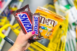 hand holding snickers candy next to m&m's