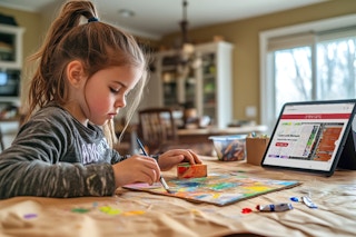 A young girl painting a craft at a kitchen table with an open ipad with Michaels online crafts on screen. 
