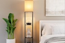 a floor lamp with shelves next to a bed