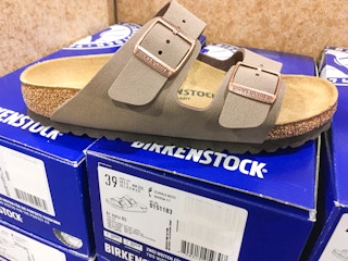 A Birkenstock sandal sitting on top of some Birkenstock shoeboxes on a shelf of a shoe store.