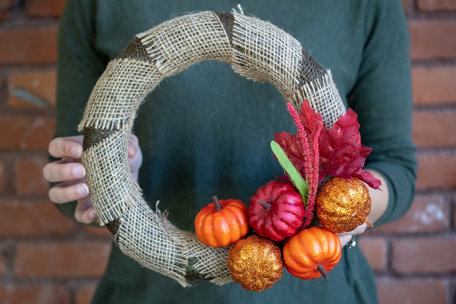 A fall wreath wrapped with burlap, adorned with pumpkins and fall leaves.