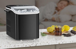 a small black ice maker on a counter next to a drink and lemons