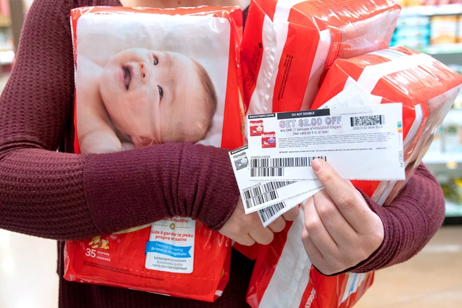 A person holding packages of baby diapers and coupons.