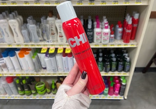 a hand holding a bottle of chi shine infusion hair spray in a store aisle
