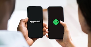 two people holding phones with the amazon music and spotify apps
