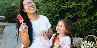 A woman laughing with her child eating popsicles and wearing Burt's Bees pajamas